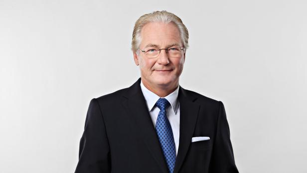 Ein Mann mit Brille, Anzug und Krawatte lächelt in die Kamera.
