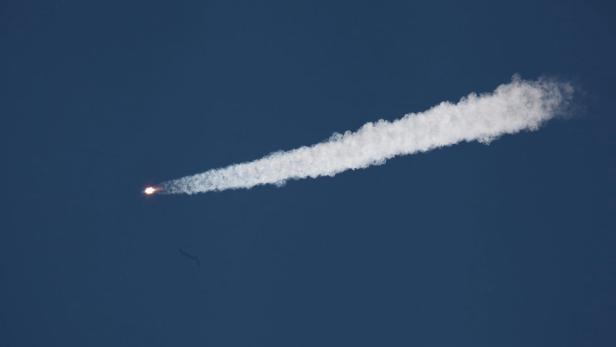 Eine Rakete steigt mit einer langen Rauchfahne in den blauen Himmel auf.
