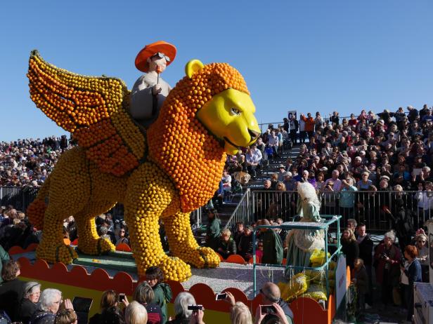 Ein Festwagen mit einem geflügelten Löwen aus Zitrusfrüchten zieht an einer Zuschauermenge vorbei.