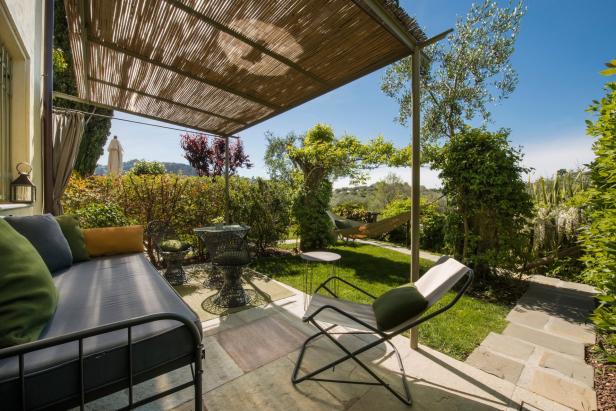 Eine überdachte Terrasse mit Liege, Stühlen und Blick in einen üppigen Garten mit Hängematte.