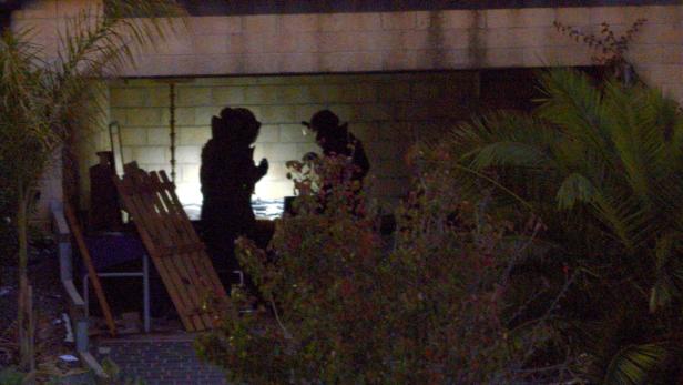 Zwei dunkel gekleidete Personen stehen im Freien vor einem Gebäude.