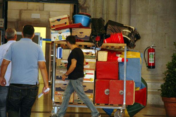 Ein Mann schiebt einen Wagen voller Kisten und anderer Gegenstände durch einen Flur.