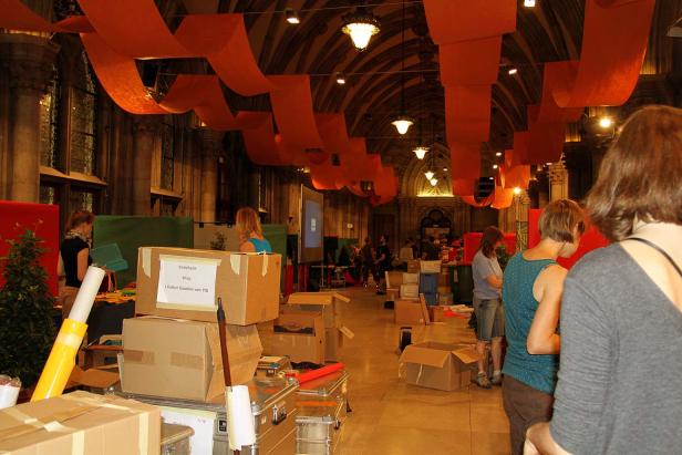 In einer Halle mit orangefarbenen Dekorationen bereiten sich Menschen auf eine Veranstaltung vor.