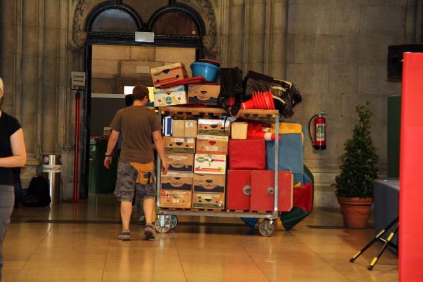 Ein Mann schiebt einen Wagen voller Kisten und Gegenstände durch ein Gebäude.