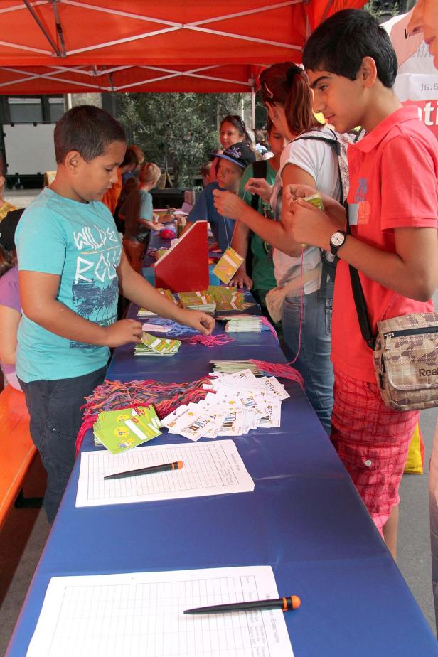 Kinder basteln an einem Stand unter einem orangefarbenen Zelt.