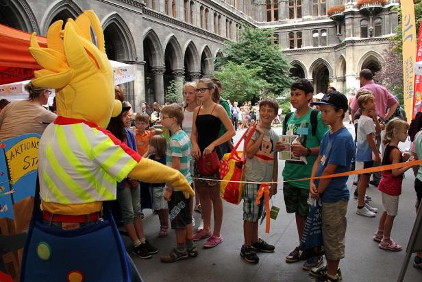 Eine gelbe Kostümfigur interagiert mit einer Gruppe von Kindern vor einem Gebäude.