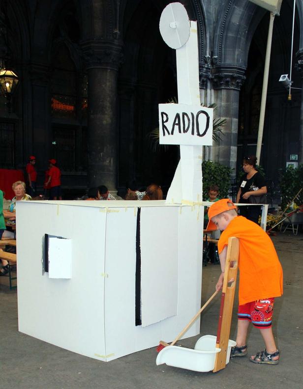 Ein Kind kehrt vor einem improvisierten Radiostudio aus Pappe.