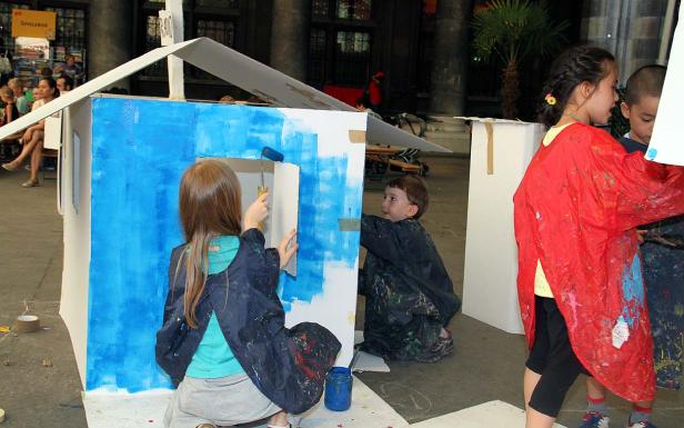 Kinder bemalen ein Papphaus mit blauer Farbe.