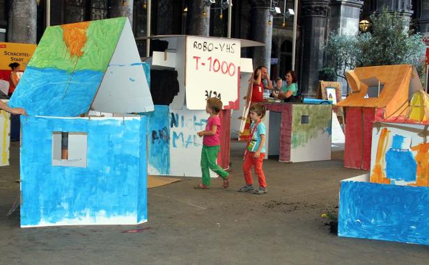 Zwei Kinder laufen durch eine „Stadt“ aus bemalten Papphäusern.