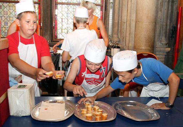 Eine Gruppe Kinder in Kochmützen bereitet belegte Brote zu.