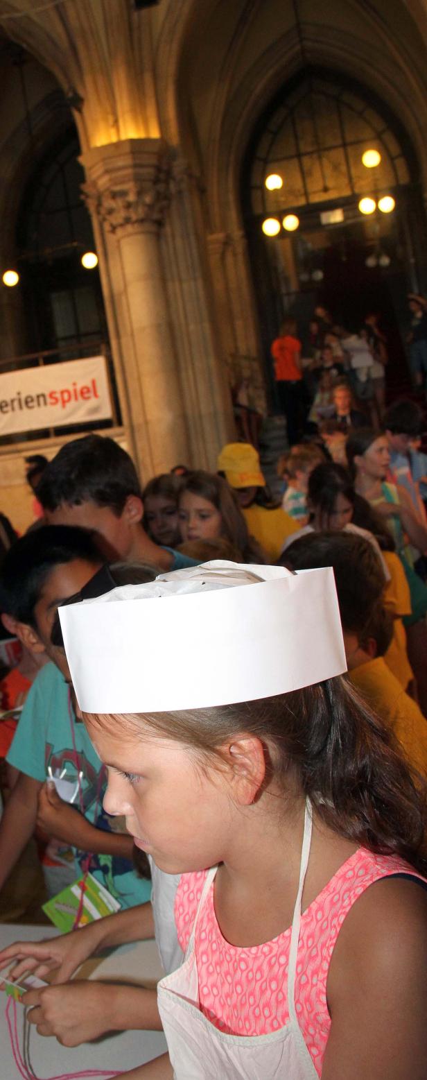 Ein Mädchen mit Kochmütze bastelt mit anderen Kindern im Hintergrund.