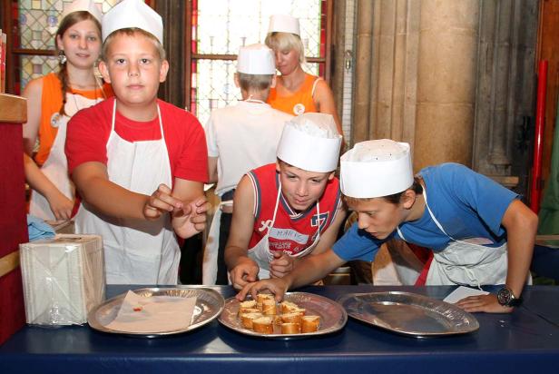 Eine Gruppe Kinder mit Kochmützen bereitet belegte Brote zu.