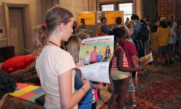Eine Gruppe von Kindern betrachtet Flyer für die Aktion „Rein ins Rathaus!“.