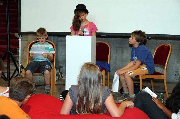 Eine junge Rednerin mit Hut steht am Rednerpult vor Publikum.