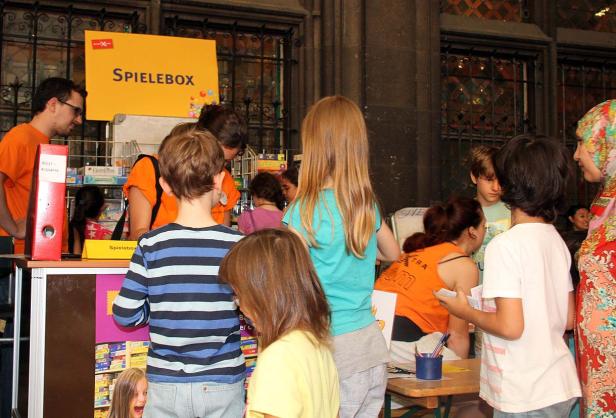 Eine Gruppe von Kindern steht an einem Stand mit der Aufschrift „Spielebox“.