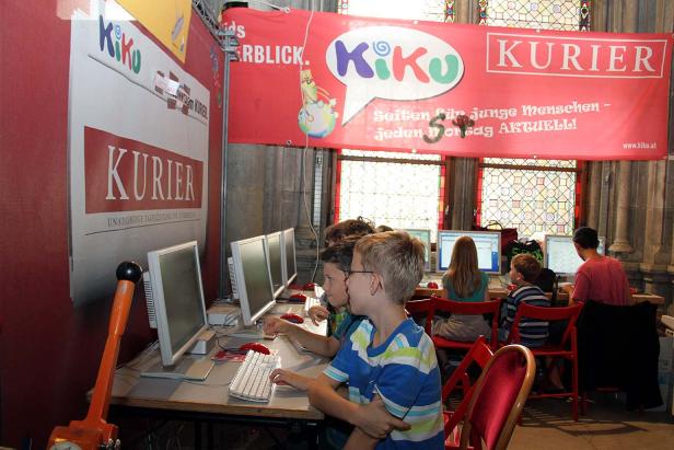 Kinder sitzen an Computern unter Bannern des „Kurier“ und „Kiku“.