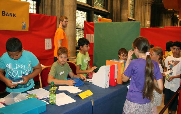 Kinder stehen an einem Stand mit der Aufschrift „Bank“.