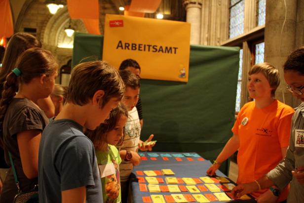 Eine Gruppe Kinder steht an einem Stand mit der Aufschrift „Arbeitsamt“.