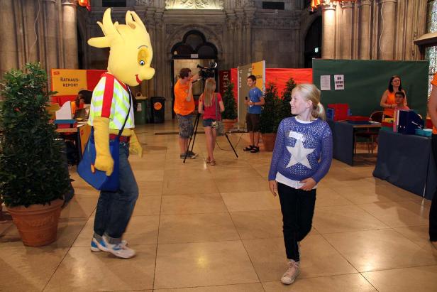 Ein Mädchen geht an einem Filmteam und einem Maskottchen vorbei.