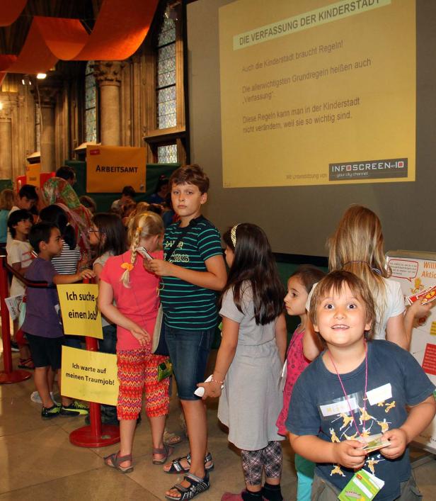 Kinder stehen in einer Schlange vor dem „Arbeitsamt“ in einer Kinderstadt.