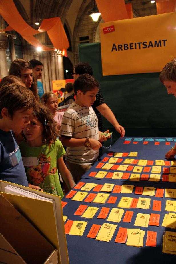 Kinder stehen an einem Stand des Arbeitsamtes und betrachten Kärtchen mit Berufsbildern.