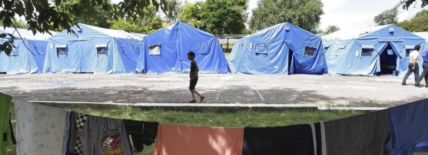 Ein Junge geht an einer Reihe blauer Zelte vorbei, im Vordergrund hängt Wäsche zum Trocknen.