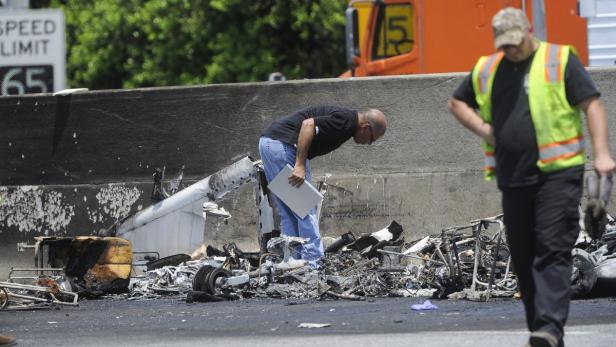 Zwei Männer begutachten die Trümmer eines Flugzeugabsturzes auf einer Autobahn.