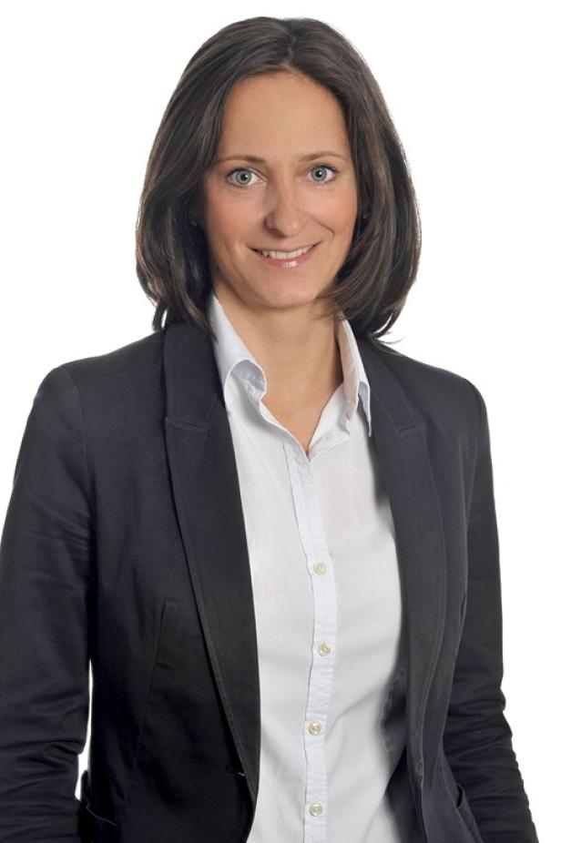 Eine Frau mit braunen Haaren und blauem Blazer lächelt in die Kamera.