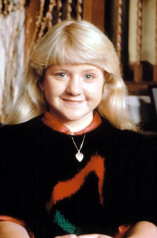Ein Porträt einer lächelnden jungen Frau mit blonden Haaren und einer Halskette mit Herzanhänger.