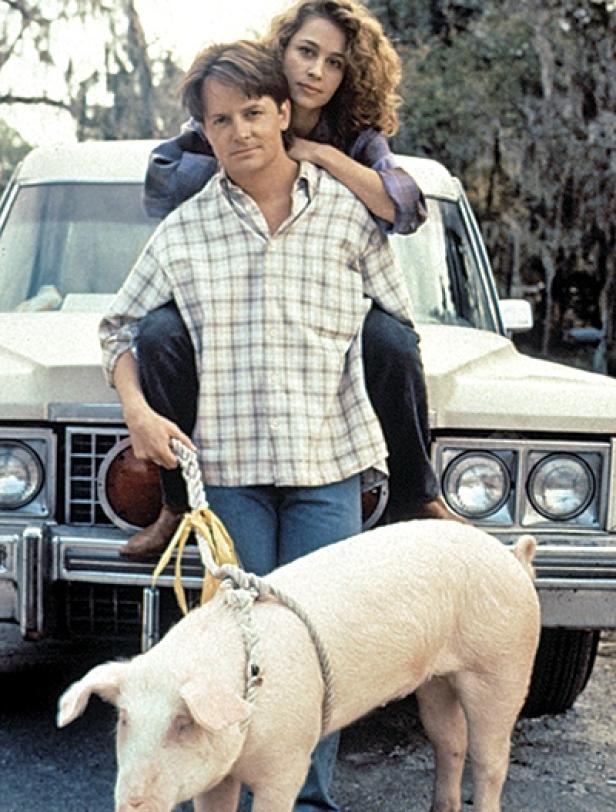 Michael J. Fox mit Frau auf dem Rücken und einem Schwein an der Leine vor einem Auto.