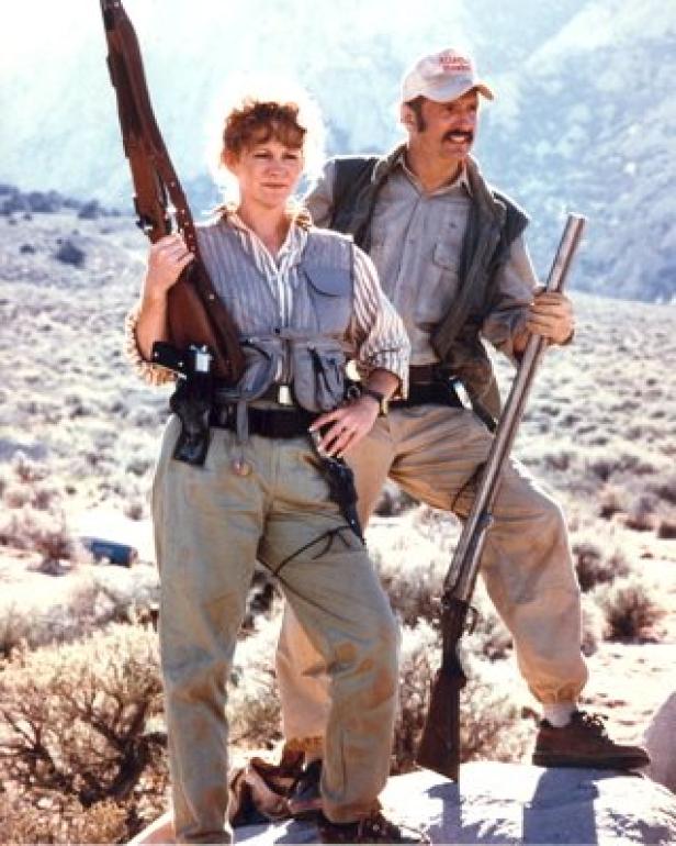 Ein Mann und eine Frau posieren mit Gewehren in einer Wüstenlandschaft.