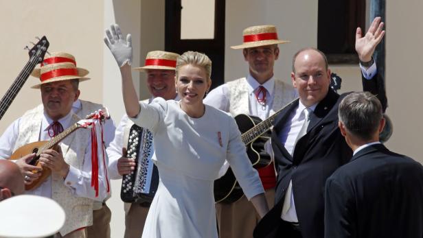 Fürst Albert II. und Fürstin Charlène von Monaco winken zusammen mit einer Musikgruppe.