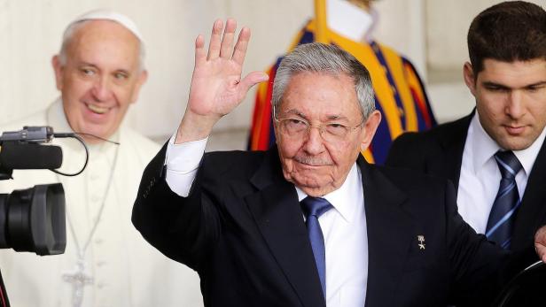 Raúl Castro grüßt, während Papst Franziskus im Hintergrund lächelt.