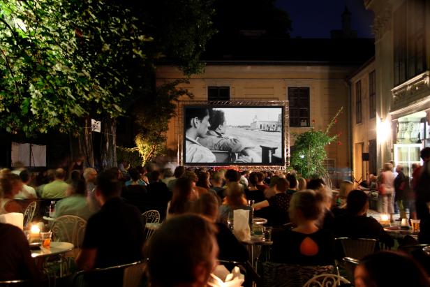 Zuschauer sitzen im Freien und schauen einen Schwarzweißfilm.