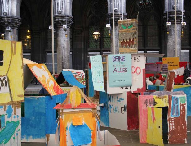 Eine Installation aus bemalten Papphäusern und Wahlplakaten in einem Innenraum.