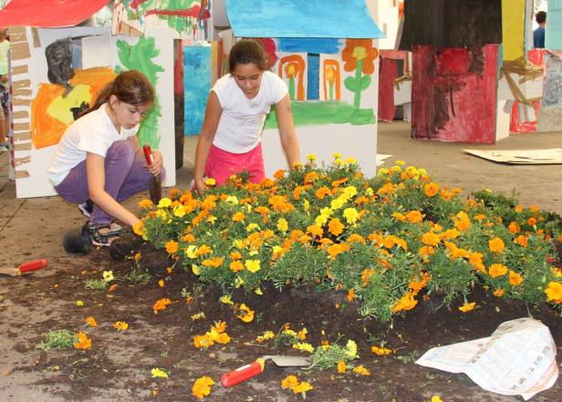 Zwei Mädchen pflanzen gelbe und orangefarbene Ringelblumen in ein Beet.