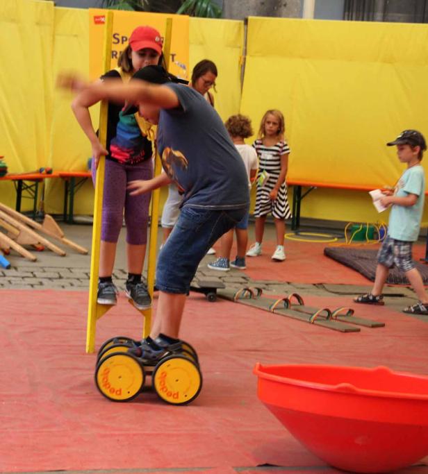 Kinder üben sich im Balancieren auf Stelzen und Rollen während eines Sportfestes.