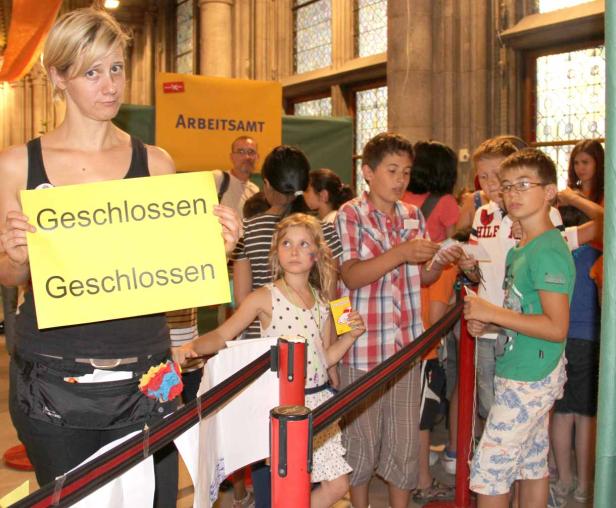 Eine Frau hält ein Schild mit der Aufschrift „Geschlossen“ vor einer Gruppe von Kindern.