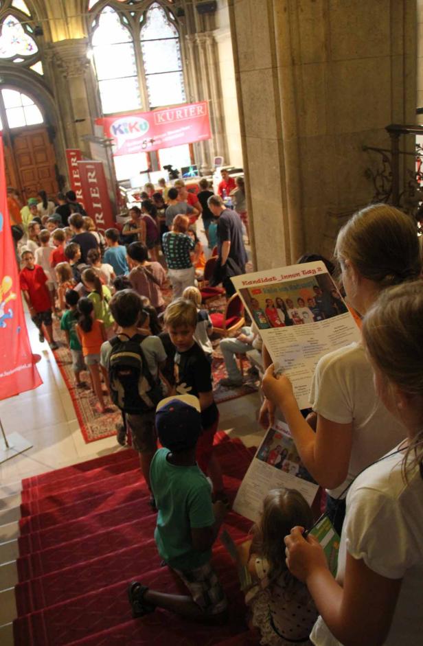 Eine Menschenmenge, darunter viele Kinder, versammelt sich in einem Gebäude mit „KiKo Kurier“-Bannern.