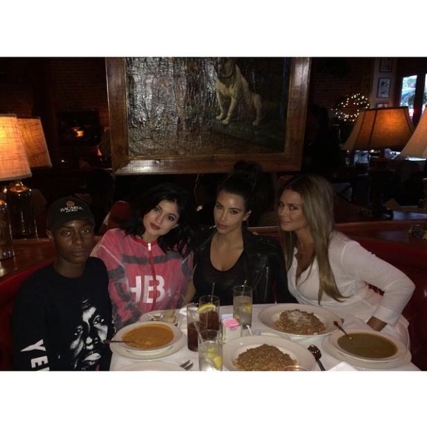 Kylie Jenner, Kim Kardashian und zwei weitere Personen sitzen an einem Tisch mit Speisen und Getränken.