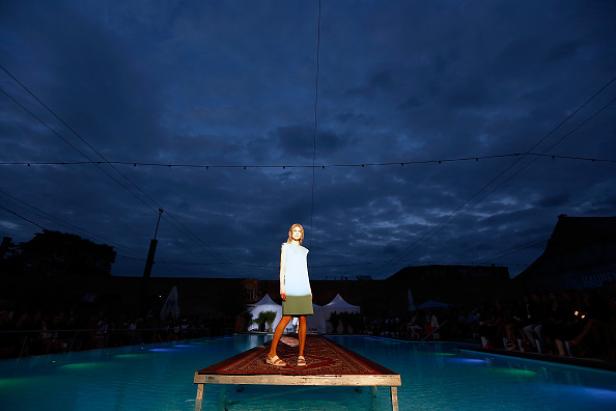 Eine Frau präsentiert ein Kleid auf einem Laufsteg, der über einen Pool führt.