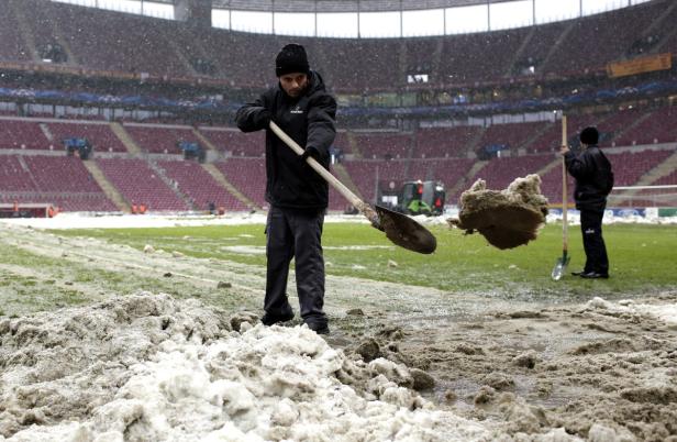 Zwei Männer schaufeln Schnee von einem Fußballfeld in einem Stadion.