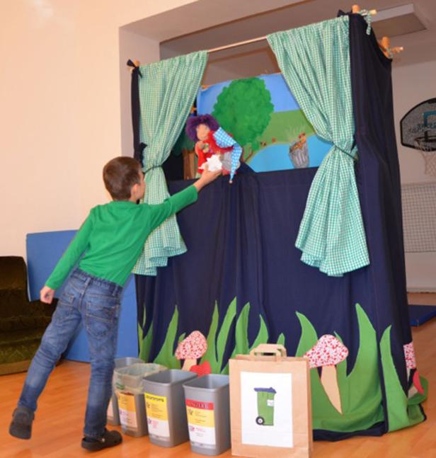 Ein Junge spielt mit einer Handpuppe vor einem selbstgebauten Puppentheater.