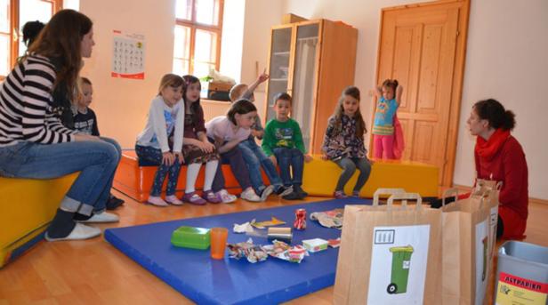 Eine Gruppe von Kindern sitzt mit zwei Erzieherinnen im Kreis und lernt etwas über Mülltrennung.