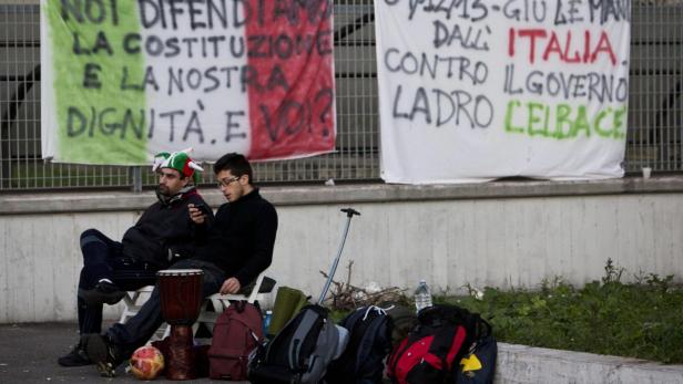 Zwei Männer sitzen vor Bannern mit italienischen Slogans.