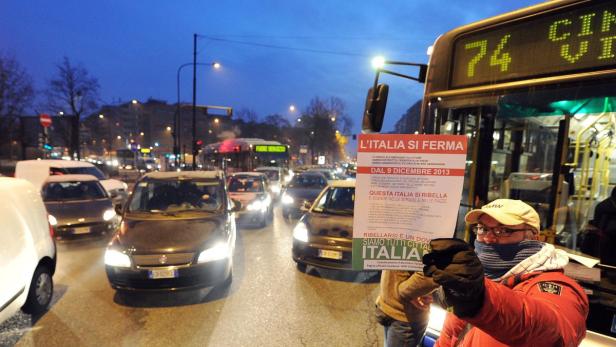 Ein Mann hält ein Schild mit der Aufschrift „L'ITALIA SI FERMA“ vor einem Bus in einer belebten Straße.