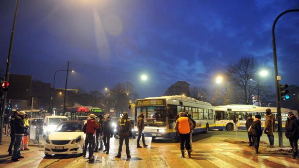 Bei Dämmerung warten Menschen an einem Zebrastreifen auf Busse.