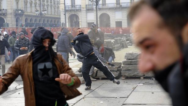Mehrere Demonstranten werfen Steine auf einem öffentlichen Platz.