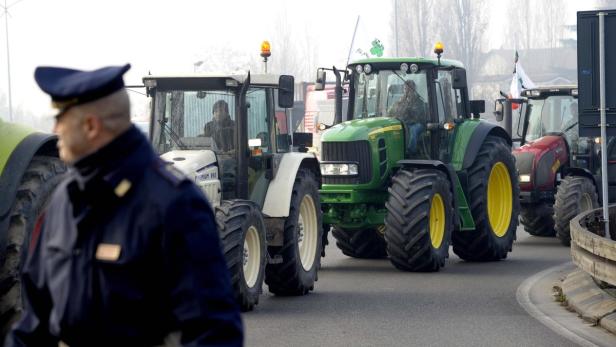 Mehrere Traktoren fahren auf einer Straße, während ein Polizist im Vordergrund steht.