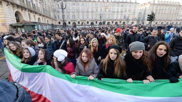 Eine Menschenmenge hält eine große italienische Flagge in einer Stadt.